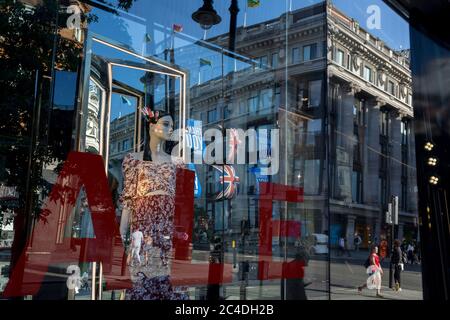 Nachdem in den letzten 24 Stunden weitere 149 Menschen an Coronavirus starben und die Todesrate in Großbritannien auf 43,320 annahmen, werden die Käufer durch das Verkaufsfenster im Geschäft „Zara“ Oxford Street verzerrt, das kürzlich das Geschäft mit Foir wieder eröffnet hat, nachdem die staatlichen Sperrregeln gelockert wurden. Die Flaggen von Union Jack hängen neben den Dankesbannern zur Unterstützung der wichtigsten Mitarbeiter des NHS (National Health Service) während der Covid-Pandemie am 25. Juni 2020 in London, England. Stockfoto