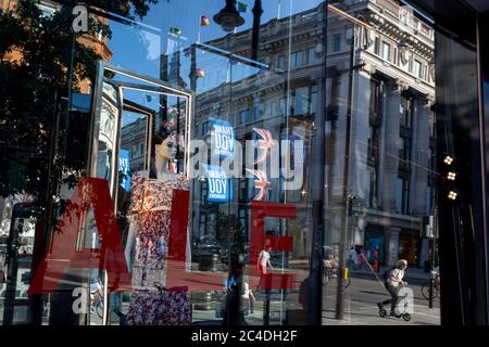 Nachdem in den letzten 24 Stunden weitere 149 Menschen an Coronavirus starben und die Todesrate in Großbritannien auf 43,320 annahmen, werden die Käufer durch das Verkaufsfenster im Geschäft „Zara“ Oxford Street verzerrt, das kürzlich das Geschäft mit Foir wieder eröffnet hat, nachdem die staatlichen Sperrregeln gelockert wurden. Die Flaggen von Union Jack hängen neben den Dankesbannern zur Unterstützung der wichtigsten Mitarbeiter des NHS (National Health Service) während der Covid-Pandemie am 25. Juni 2020 in London, England. Stockfoto