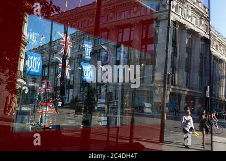 Nachdem in den letzten 24 Stunden weitere 149 Menschen an Coronavirus starben und die Todesrate in Großbritannien auf 43,320 annahmen, werden die Käufer durch das Verkaufsfenster im Geschäft „Zara“ Oxford Street verzerrt, das kürzlich das Geschäft mit Foir wieder eröffnet hat, nachdem die staatlichen Sperrregeln gelockert wurden. Die Flaggen von Union Jack hängen neben den Dankesbannern zur Unterstützung der wichtigsten Mitarbeiter des NHS (National Health Service) während der Covid-Pandemie am 25. Juni 2020 in London, England. Stockfoto