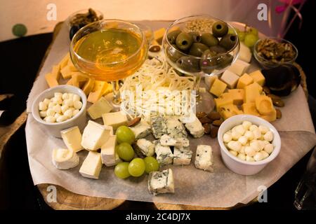 Käse mit Honig, Trauben und grünen Oliven auf Käseplatte oder Holzbrett. Feinkostgeschäft oder leckere Vorspeisen Konzept Stockfoto