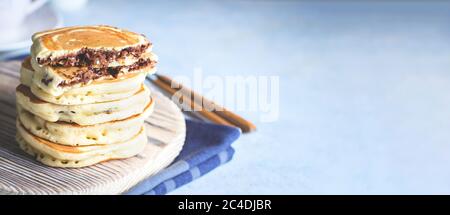 Stapel gefüllter Schokolade Nutella Pfannkuchen auf Holzbrett auf blauen Tisch Hintergrund. Amerikanisches Frühstückskonzept. Speicherplatz kopieren. Banner für Website Stockfoto