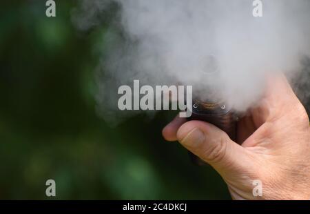 Eine Nahaufnahme der Hand eines Mannes, der eine E-Zigarette hält / verdampft Mod, wie er vapes Erstellen viel vape Nebel Stockfoto