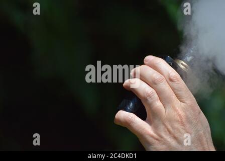 Eine Nahaufnahme der Hand eines Mannes, der eine E-Zigarette hält / verdampft Mod, wie er vapes Erstellen viel vape Nebel Stockfoto