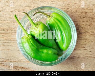 Frische grüne Chilischoten in einer Glasschale mit Ramekin, die auf einem Holzbrett zentriert ist Stockfoto