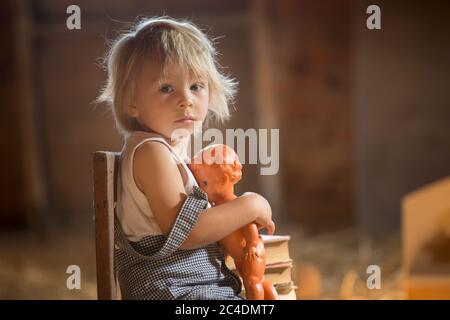 Kleiner Kleinkind Junge, sitzt auf alten Vintage Bank, hält Puppe und spielt auf dem Dachboden Stockfoto