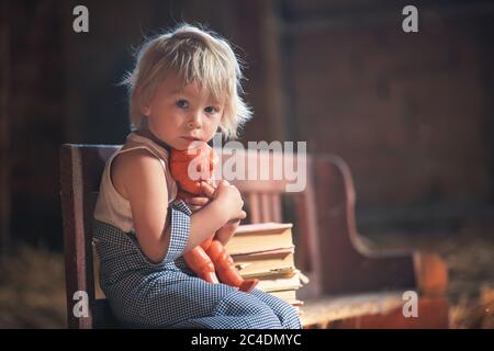 Kleiner Kleinkind Junge, sitzt auf alten Vintage Bank, hält Puppe und spielt auf dem Dachboden Stockfoto