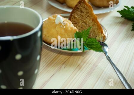 Portion Kuchen, eclair gefüllt mit Schlagsahne mit einer Tasse Tee auf einem hölzernen Hintergrund. Stapeln Sie Pudding Cookies und Tee. Eclairs auf Platte und ein schwarz Stockfoto