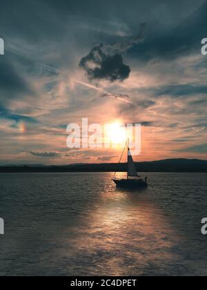 Segelboot bei Sonnenuntergang auf ruhigen Meer wolkigen Himmel Stockfoto