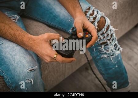 Männliche Hände, die den Joystick halten. Moderner junger Mann in Jeans verbringt Zeit mit Computerspiel. Lifestyle-Konzept. Nahaufnahme. Getöntes Bild Stockfoto