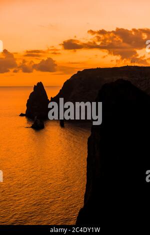 Ein rot brennender Sonnenuntergang mit dem Silhouett einer Klippe über dem Meer Stockfoto