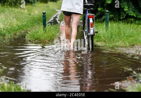 Berlin, Deutschland. Juni 2020. Nach heftigen Regenschauern schiebt ein Radfahrer ihr Fahrrad durch eine große Pfütze. Quelle: Jens Kalaene/dpa-Zentralbild/dpa/Alamy Live News Stockfoto
