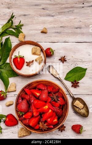 Zutaten zum Kochen Erdbeermarmelade. Reife Beeren, brauner Zucker, frische Minze, duftende Gewürze. Rustikale Holzbretter Hintergrund, Draufsicht Stockfoto