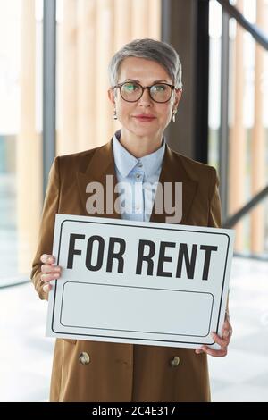 Portrait der reifen Geschäftsfrau in Brillen halten Plakat für Miete in ihren Händen, während sie im Büro stehen Stockfoto