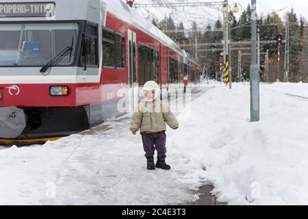 STRBSKE PLESO, SLOWAKEI - 1. NOVEMBER 2017: Glücklicher Kleinkind Junge neben Poprad Tatry Zug in verschneiten Bahnhof von Strbske Pleso in Slovaki Stockfoto