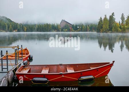 Nebliger Herbst Strbske See mit Rückbau und roten Booten im Vordergrund auf dem Wasser im Nationalpark hohe Tatra, Slowakei Stockfoto