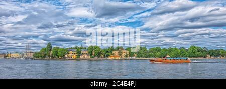 STOCKHOLM SCHWEDEN - 2. AUGUST 2019: Panoramablick auf die Küste der Insel Skeppsholmen mit Booten und Schiffen und bewölktem Himmel Stockfoto