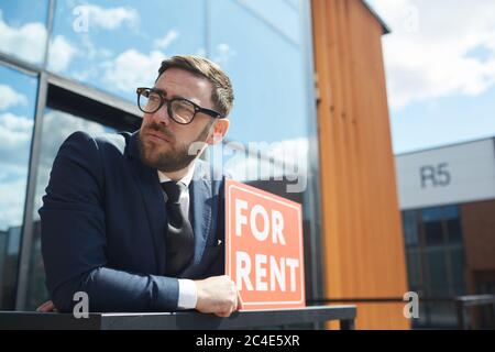 Reifer bärtiger Mann in Anzug hält Plakat und steht im Freien in der Nähe des Bürogebäudes Stockfoto
