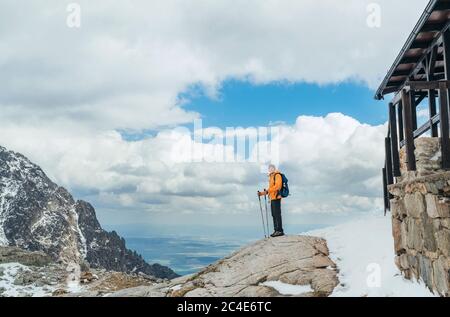 Gekleidet leuchtend orange Jacke Backpacker Wandern in der Hohen Tatra Bergkette, Slowakei mit Trekkingstöcken. Wanderer, der in der Nähe der Berghütte um 2015 steht Stockfoto