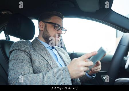Reife bärtige Mann mit digitalen Tablet er arbeitet online im Auto Stockfoto