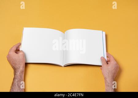 Männliche Hände mit einem geöffneten Buch-Katalog mit leeren Seiten auf gelbem Hintergrund, Modell-Serie Vorlage bereit für Ihre Design-Seiten Auswahl Pfad in Stockfoto