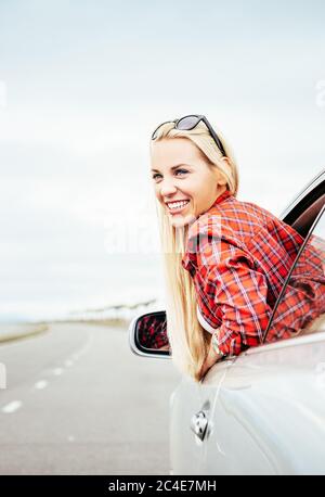 Glücklich lächelnde junge Frau schaut aus dem Autofenster Stockfoto