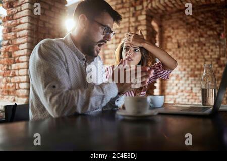 Junge kaukasische Paar Blick auf Laptop vor ihnen, schlechte Nachrichten erhalten, Fehler gemacht, Kaffee trinken im Café Stockfoto