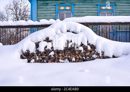 Mit Schnee gestapeltes Brennholz vor einem alten russischen Haus Stockfoto
