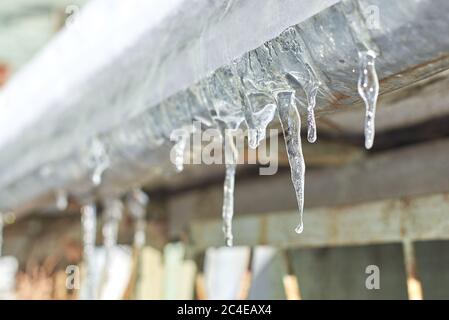 Kleine schmelzende Eiszapfen hängen an einem klaren Wintertag auf dem Gebäude Stockfoto