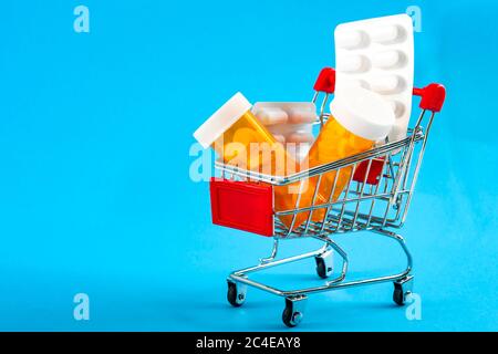 Shopping für Medikamente, Gesundheitskosten und verschreibungspflichtige Medikamente Konzept mit einem Warenkorb oder Trolley mit Pillen isoliert auf einem blauen Rücken gefüllt Stockfoto