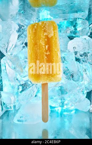 Ein erfrischendes Dessert, gelber Fruchtpopsicle mit dem Geschmack von reifen Mango liegt auf Eisstücken Stockfoto