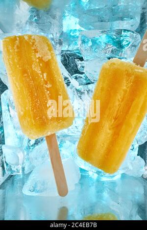 Ein erfrischendes Dessert, gelber Fruchtpopsicle mit dem Geschmack von reifen Mango liegt auf Eisstücken Stockfoto