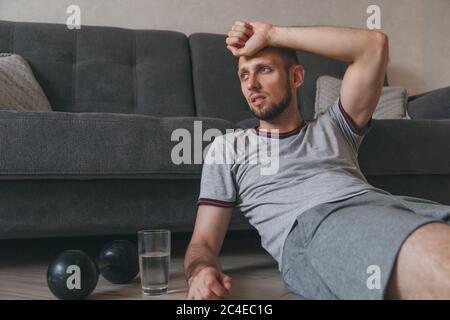 Müde nach dem Training und Training. Übertraining zu Hause während der Selbstisolation. Erschöpfter Mann sitzt auf dem Boden Atmung und Ruhe nach schweren Herz Stockfoto