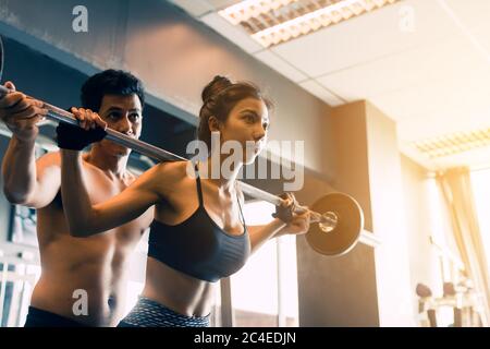 Personal Trainer hilft Frauen und Griff schwere Langhanteln zwei Hand oben eine Schulter. Stockfoto