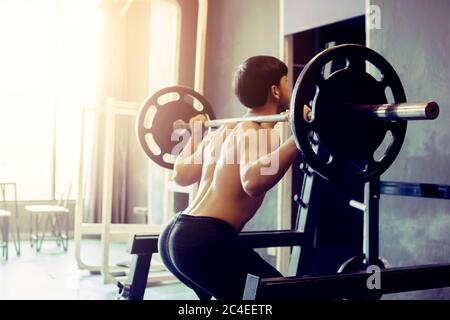 Rückansicht des asiatischen Mannes Durchführung Langhantel hockt im Indoor-Fitness-Studio. Stockfoto