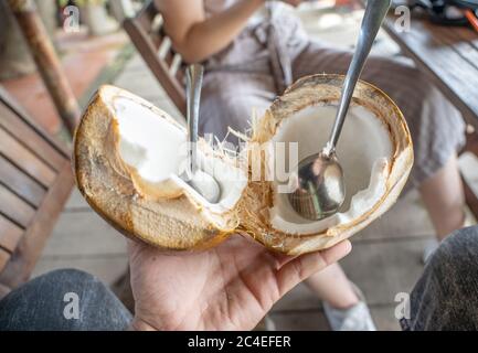 Selektive Fokusaufnahme einer männlichen Hand, die eine geöffnete hält Kokosnuss mit Löffeln Stockfoto