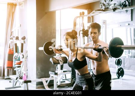 Personal Trainer hilft Frauen und Griff schwere Langhanteln zwei Hand oben eine Schulter. Stockfoto