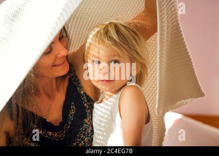 Mutter und Kind, Spaß zusammen, sitzen auf dem Bett, Schatten von der Sonne und die Decke fallen auf ihre Gesichter und lassen schöne Zeichnung Stockfoto