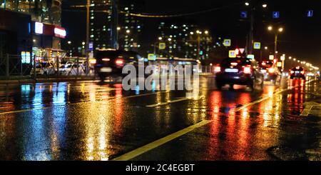 Regnerische Nacht in der Stadt. Nasse Straße, Autos, farbige Lichtreflexe und verschwommene Silhouetten Stockfoto