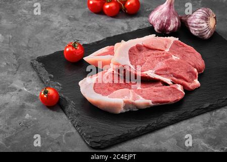 Zwei Stücke Schweinefleisch auf einem Schieferteller auf einem grauen Hintergrund. Kopierraum, Foto für Lebensmittelgeschäfte Stockfoto