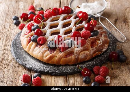 Hausgemachte offene Beerenpastete mit Himbeeren, Heidelbeeren und Kirschen aus der Nähe auf einem Schieferbrett auf dem Tisch. Horizontal Stockfoto