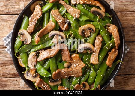 Asiatisches Rindfleisch mit Champignons und Schoten aus grünen Erbsen, Sesamsamen in Nahaufnahme auf einem Teller auf dem Tisch. Horizontale Draufsicht von oben Stockfoto