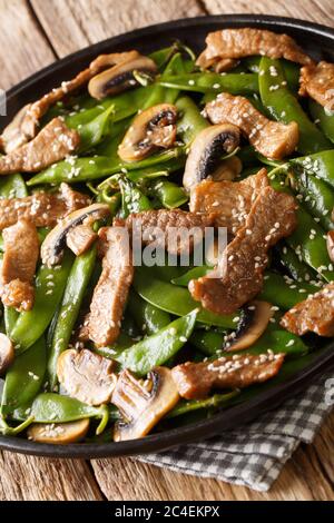 Braten Sie Rindfleisch mit Pilzen und Schoten von grünen Erbsen, Sesam in einer Platte auf dem Tisch. Vertikal Stockfoto