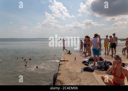 Leigh-on-Sea, Großbritannien. Juni 2020. Menschen genießen warmes Wetter am Bell Wharf Beach, Leigh-on-Sea, Essex. Schwimmer im Wasser, Sonnenanbeter auf der Betonplattform und eine Person mitten im Sprung fangen einen lebendigen Moment der Sommererholung ein. Die Leute springen von der Bell Wharf ins kühle Wasser. Leute in Old Leigh, Essex, genießen das warme Wetter und weniger überfüllte Strände. Penelope Barritt/Alamy Live News Stockfoto
