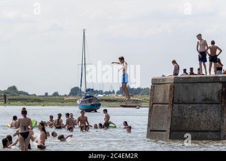Leigh-on-Sea, Großbritannien. Juni 2020. Menschen schwimmen und springen vom Betonsteg am Bell Wharf Beach, Leigh-on-Sea, Essex. Ein Segelboot liegt vor der Küste, mit Bäumen und Uferlinien im Hintergrund. Fängt Sommerurlaub und Engagement in der Gemeinschaft ein. Die Leute springen von der Bell Wharf ins kühle Wasser. Leute in Old Leigh, Essex, genießen das warme Wetter und weniger überfüllte Strände. Penelope Barritt/Alamy Live News Stockfoto