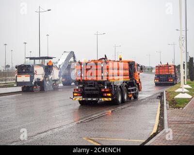 Der Straßenfräser entfernt den Asphalt von der Straße und die Bewässerungsmaschine spült die Reste weg. Straßenarbeiten sind im Gange. Stockfoto