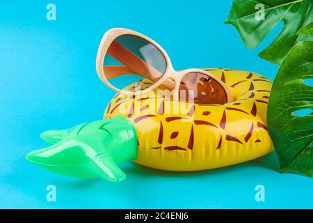 Aufblasbare Ananas auf blauem Hintergrund mit Sonnenbrille und Monstera-Blättern. Sommerkonzept Urlaub. Hintergrund für den Verkauf. Stockfoto