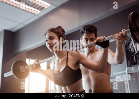 Personal Trainer hilft Frauen und Griff schwere Langhanteln zwei Hand oben eine Schulter. Stockfoto