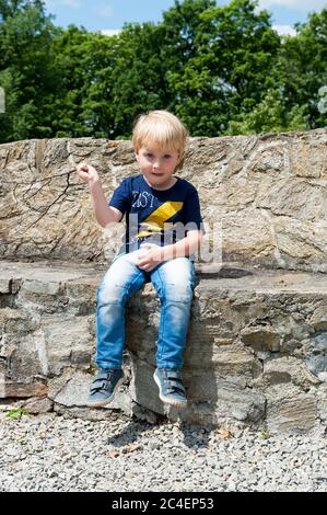 Dreijähriger Junge sitzt auf einer Mauer neben dem Schloss in Kamieniec Ząbkowicki, Kreis Ząbkowice Śląskie, Woiwodschaft Niederschlesien, Polen Stockfoto