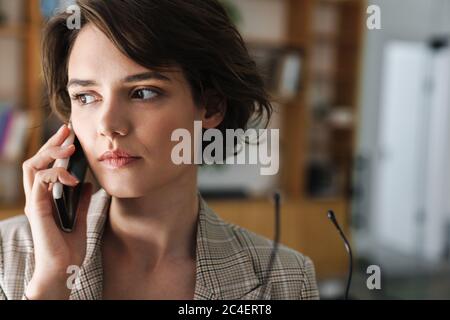 Schöne ernsthafte junge Geschäftsfrau im Büro stehend, mit Handy Stockfoto