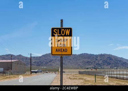 Apple Valley, CA / USA – 16. Mai 2020: Ein gelb-schwarzes Straßenschild die liest langsam Sharp Turn ahead befindet sich in Apple Valley, Kalifornien. Stockfoto